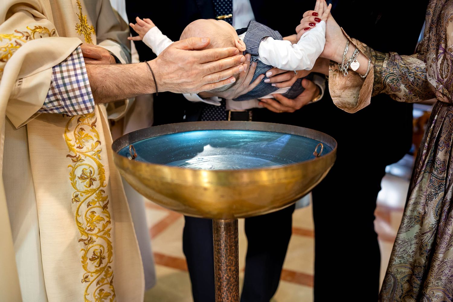 Close-up of infant being baptized over golden font by priest during Catholic christening ceremony.