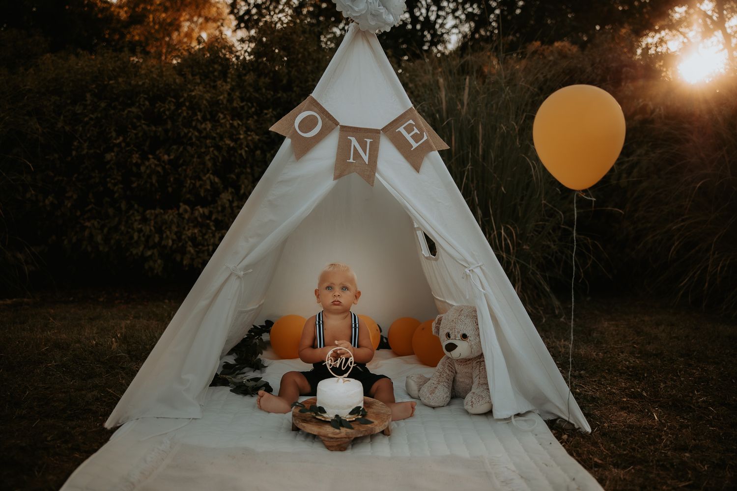White teepee tent decorated with stuffed animals and orange balloons for a photo session.