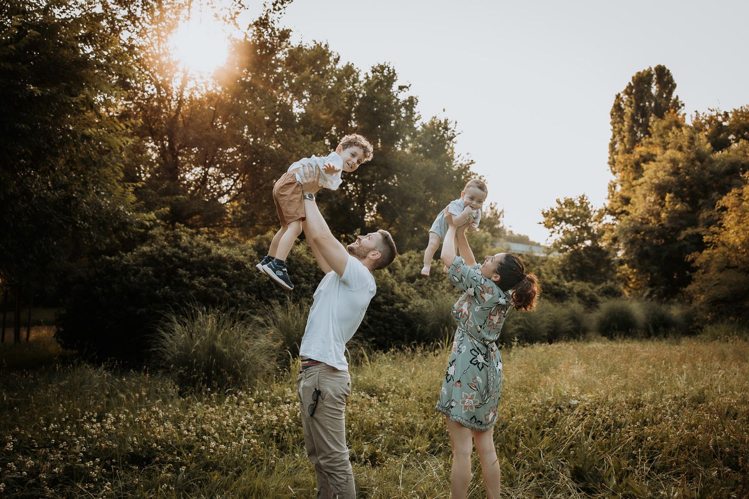 Family playing and dancing together in a sunlit meadow at sunset.