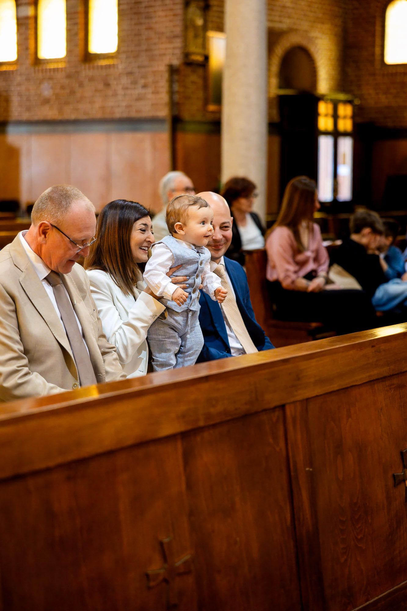 Family with baby smiling in church pew during baptism ceremony, grandparents and mother holding infant.