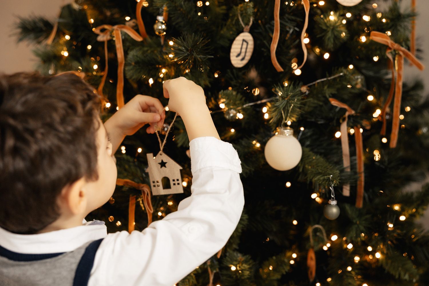 Young boy decorating a Christmas tree with ornaments, ribbons, and warm glowing lights.