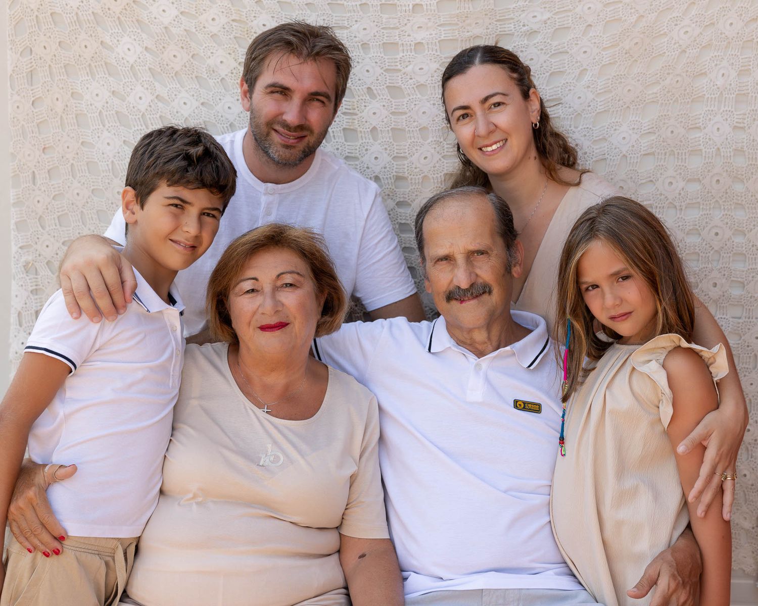 Multi-generational family of six posing together outdoors, smiling warmly in casual light-colored outfits.