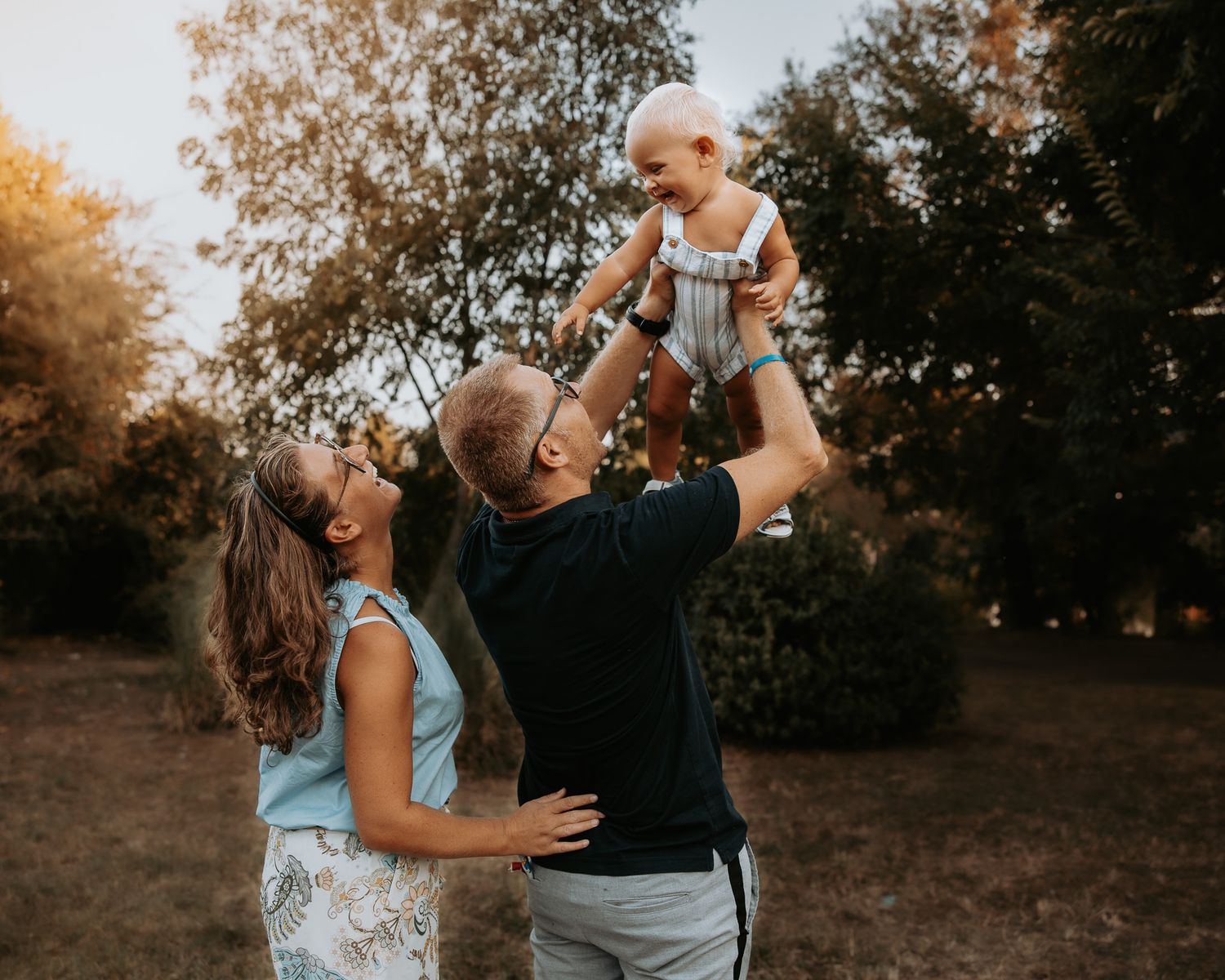 Family playing and laughing together in a park during golden hour.