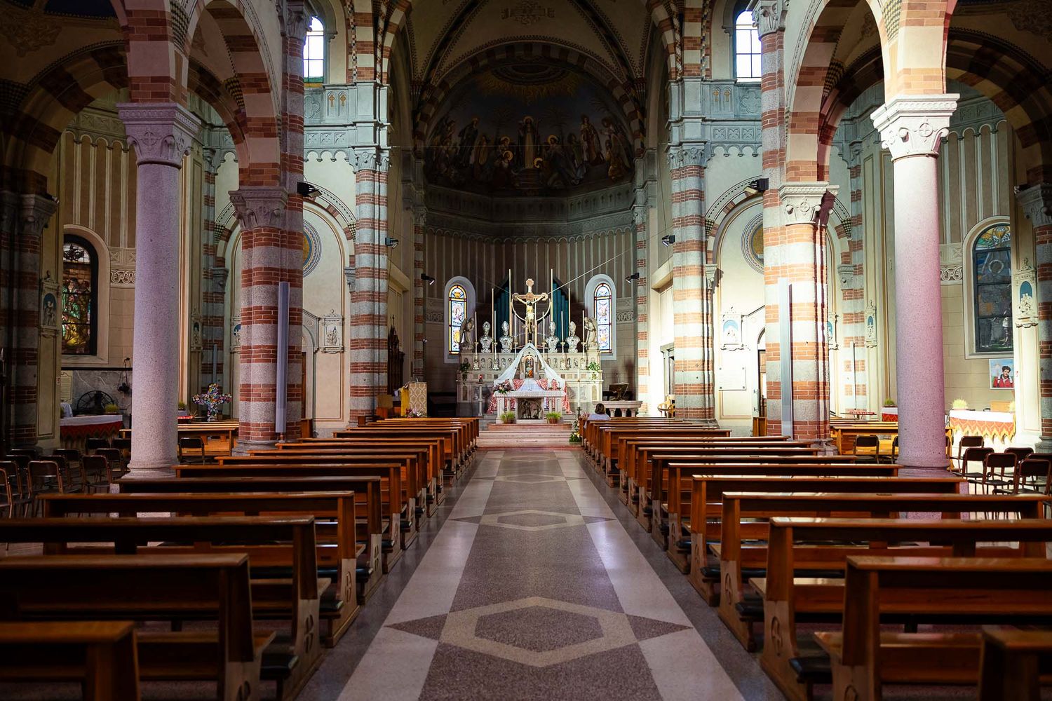 Interior of a grand cathedral with ornate striped columns, wooden pews, and a decorated altar bathed in natural light.