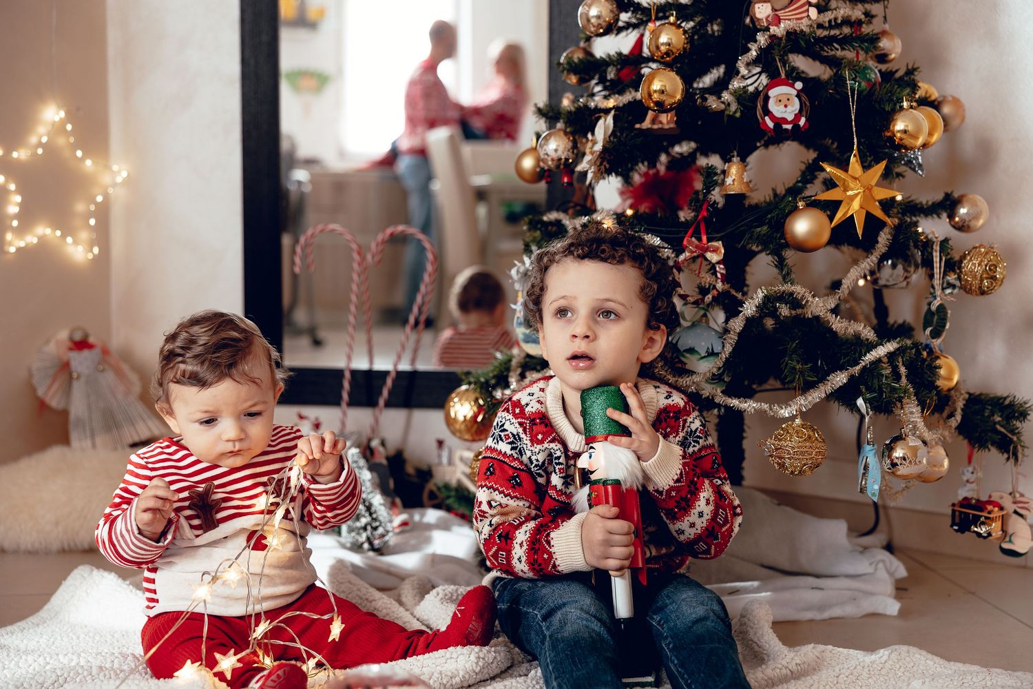 Children sit near decorated Christmas trees and holiday lights while opening presents and enjoying festive moments.