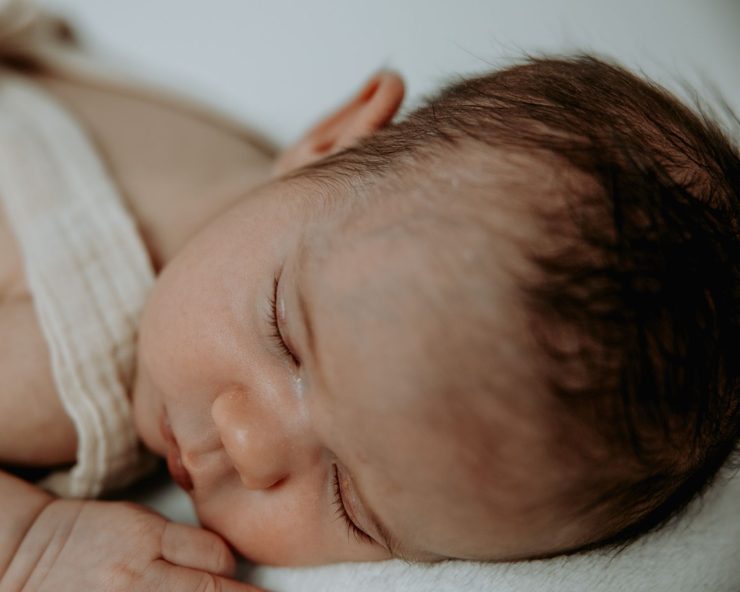 A sleeping newborn baby lies peacefully on white bedding in a series of close-up shots.