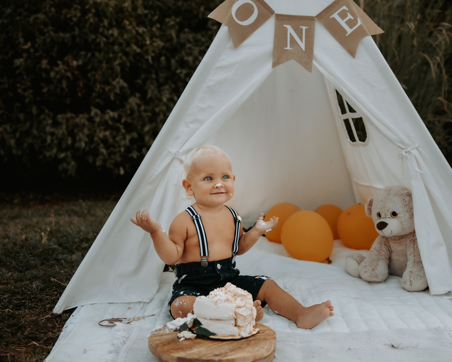 Festive birthday setup with white teepee, orange balloons, and 'ONE' banner.