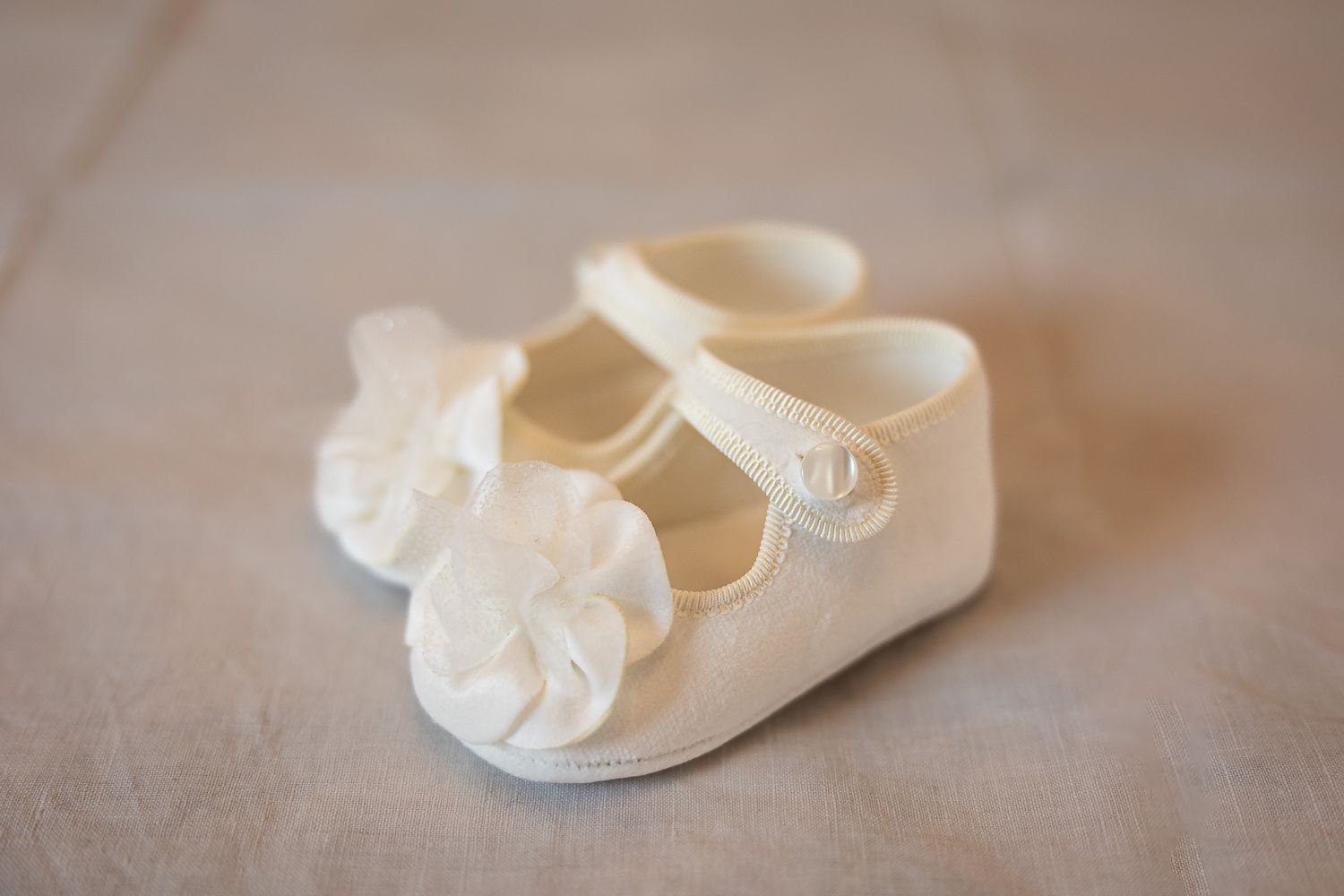 White baby girl Mary Jane shoes with flower detail on a soft background.