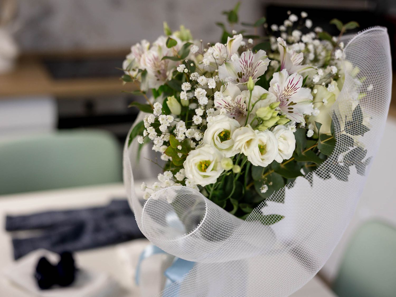 Elegant white bouquet with alstroemeria, lisianthus, and baby's breath wrapped in sheer white mesh ribbon on a table.