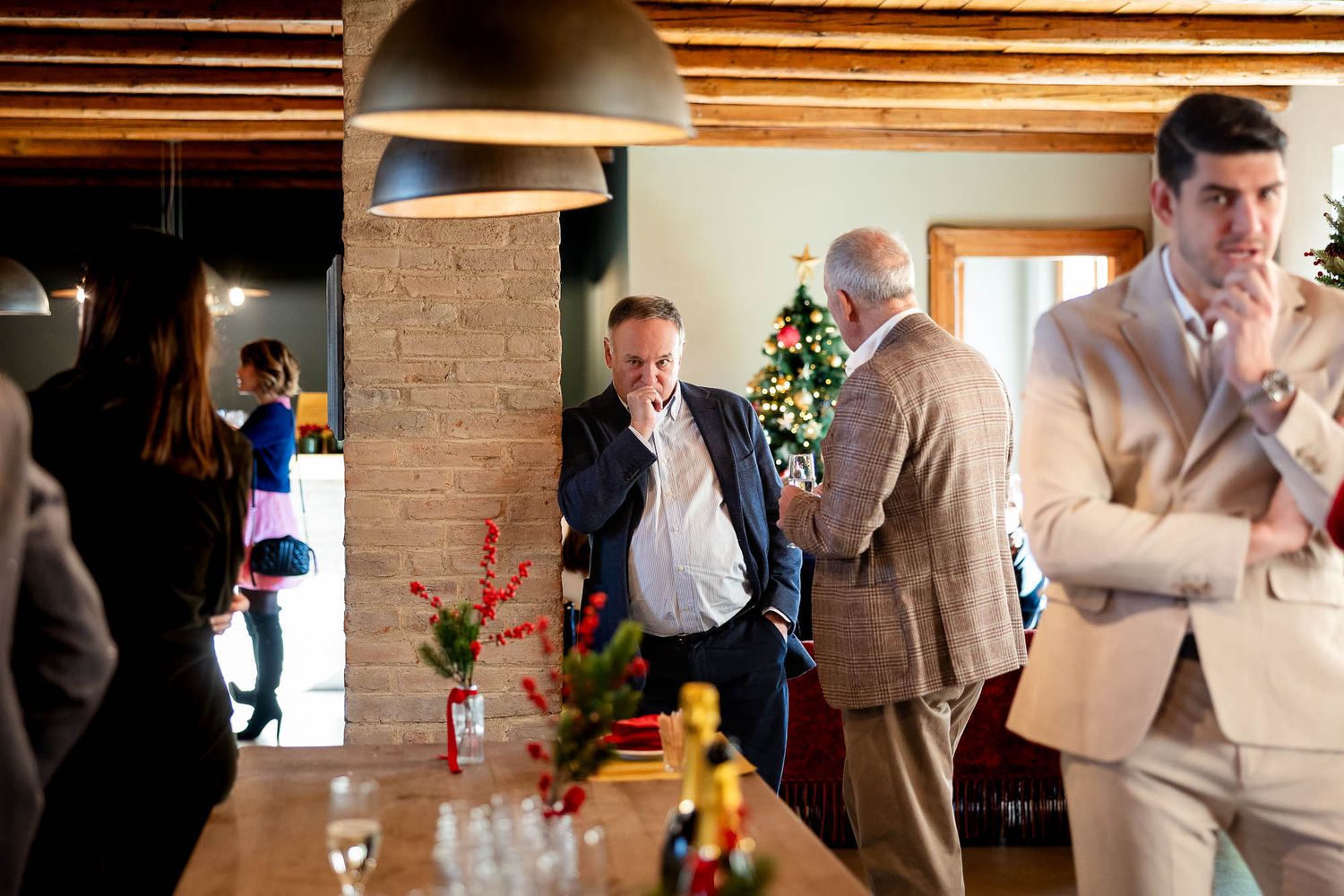 Professionals networking at a festive holiday office party with Christmas tree and seasonal decorations indoors.