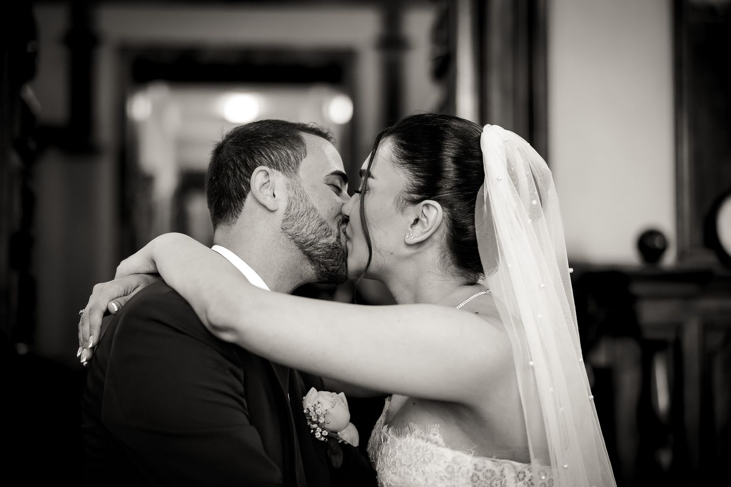 Black and white wedding photo of bride and groom sharing a romantic first kiss, bride wearing veil and lace gown.