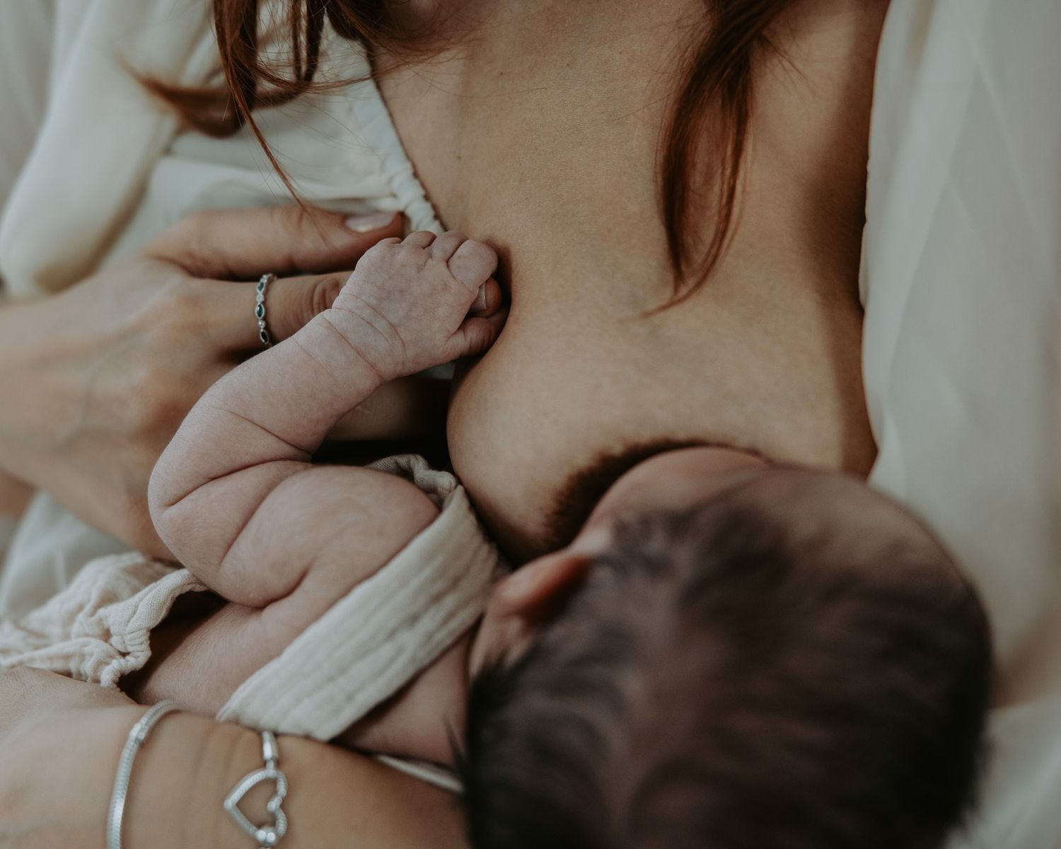 A mother breastfeeding her baby in a tender moment captured in warm, natural lighting.