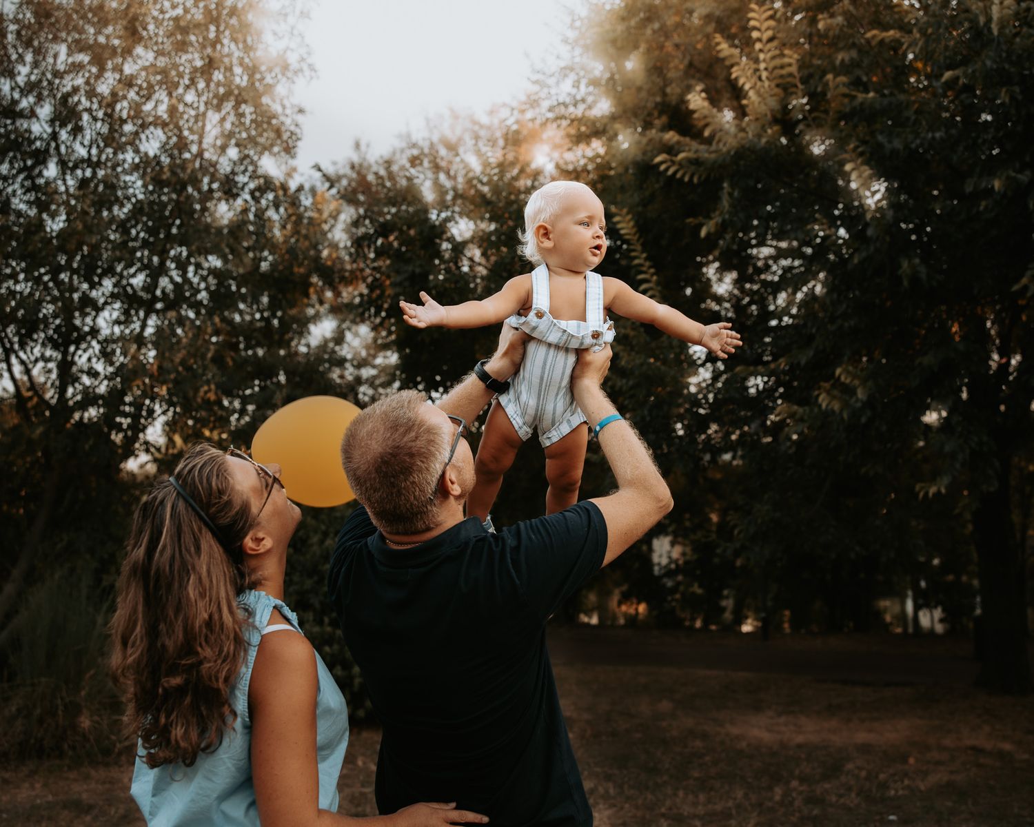 Candid family moment captured outdoors during golden hour with trees in background.