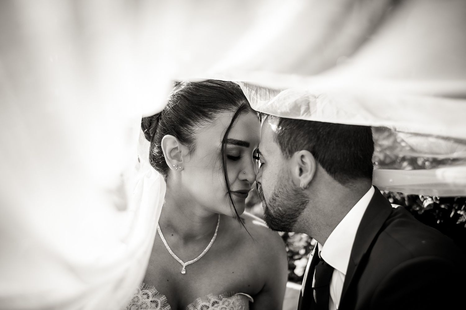 Black and white wedding photo of bride and groom sharing an intimate moment under a veil.