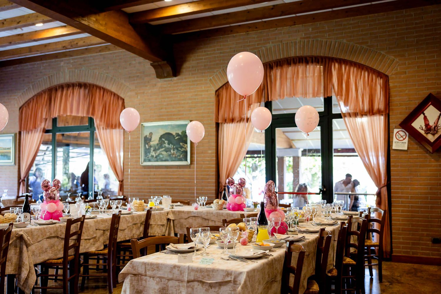 Restaurant dining room with pink balloon decorations and arched windows set for a birthday party.