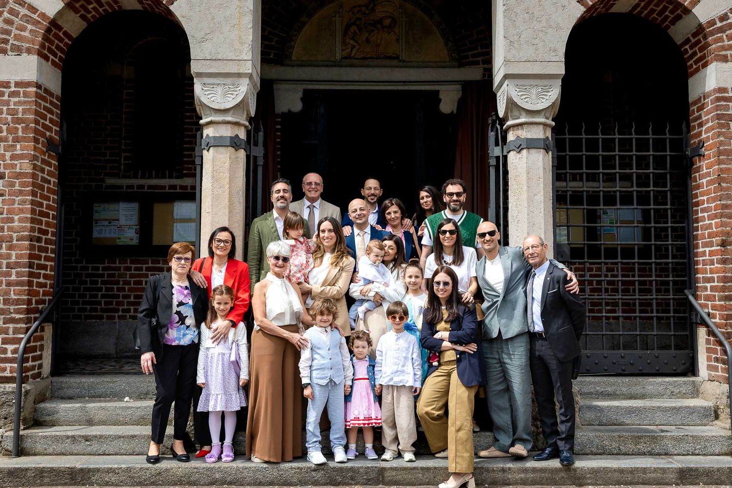 Large family group posing on church steps for a special occasion, dressed in elegant attire for a celebration.