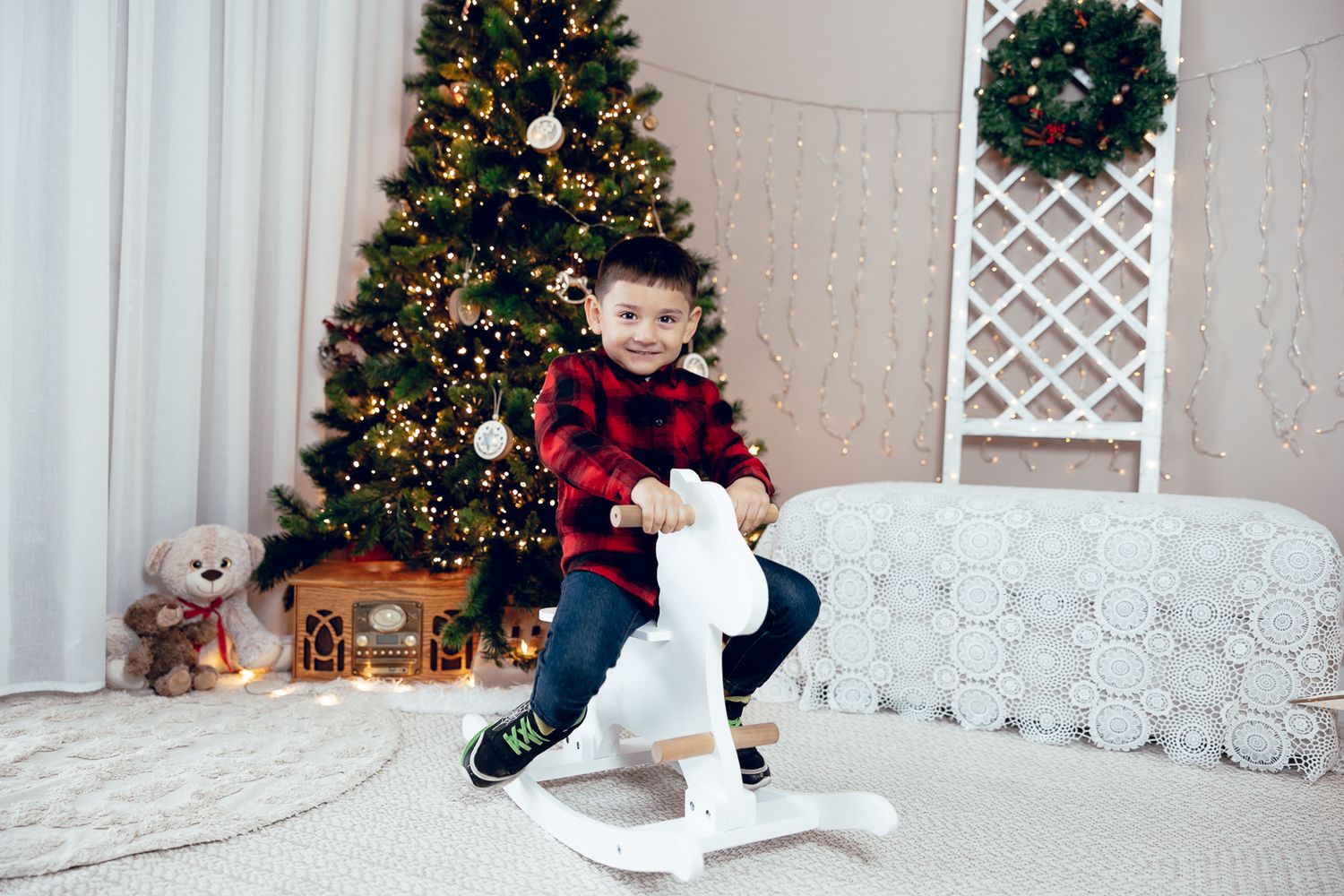 A festive Christmas scene with decorated trees and white lattice decorations against a beige wall.