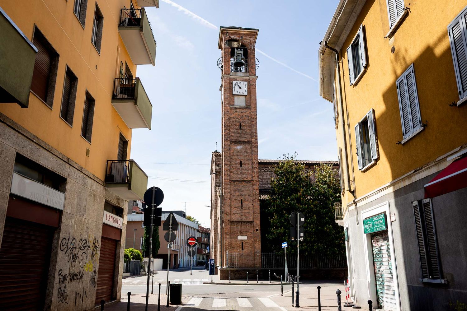 Tall brick bell tower rising above colorful Italian street buildings under a clear blue sky.