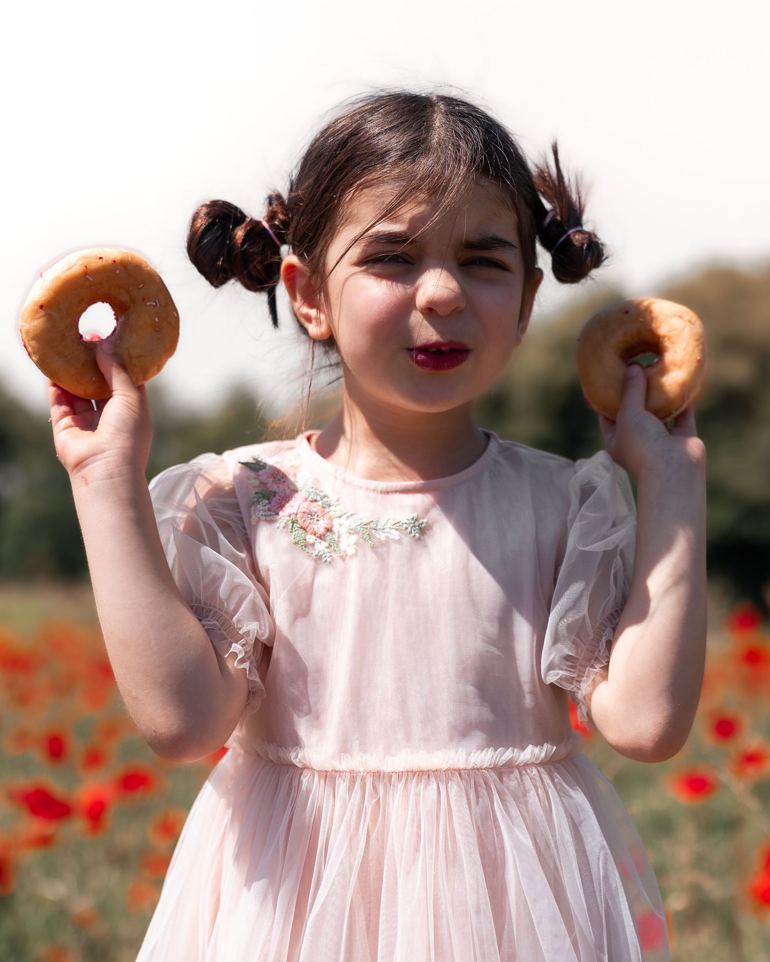 Joyful moment captured in poppy field with pink donuts and white dress.