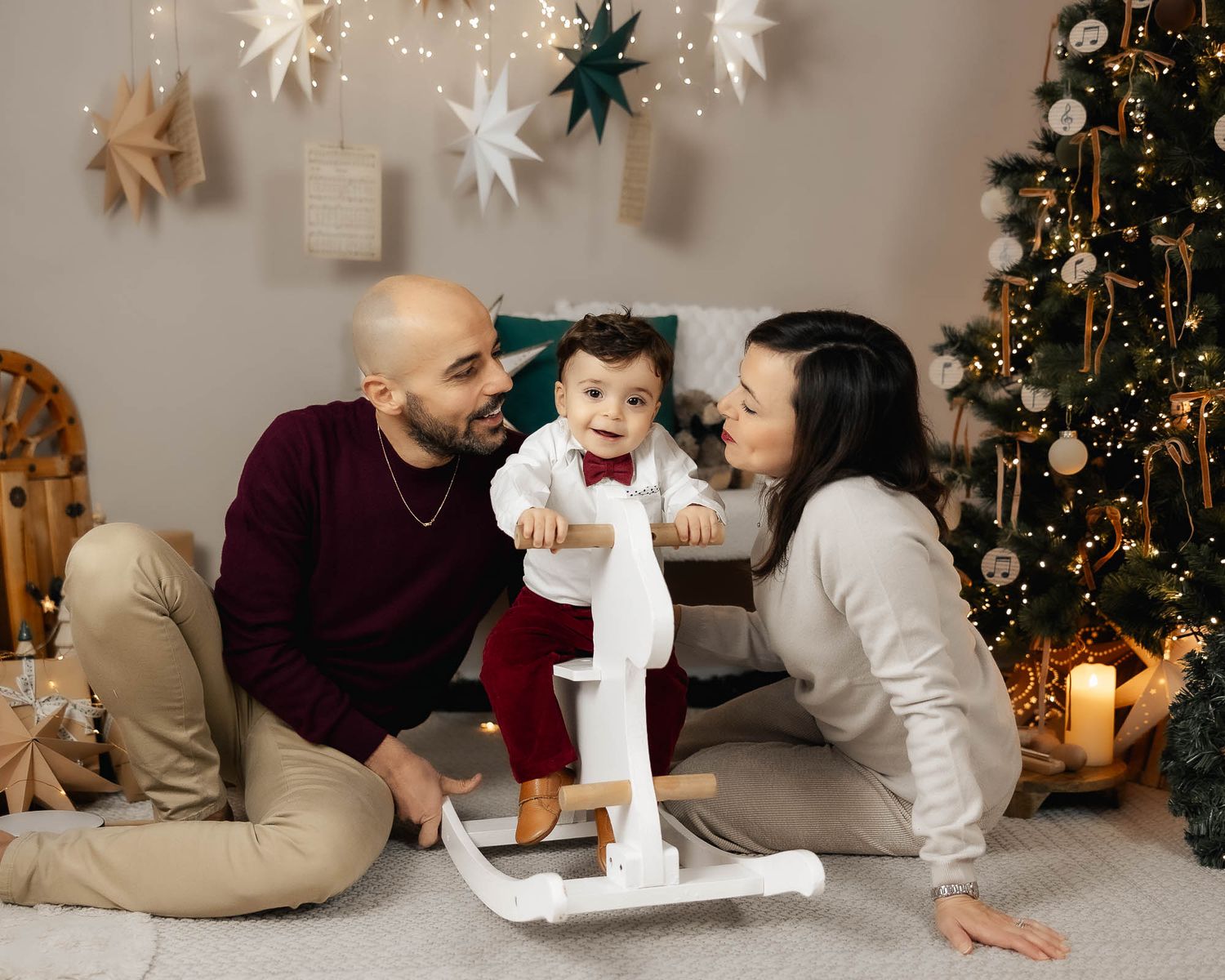 Family with baby celebrating Christmas near decorated tree.
