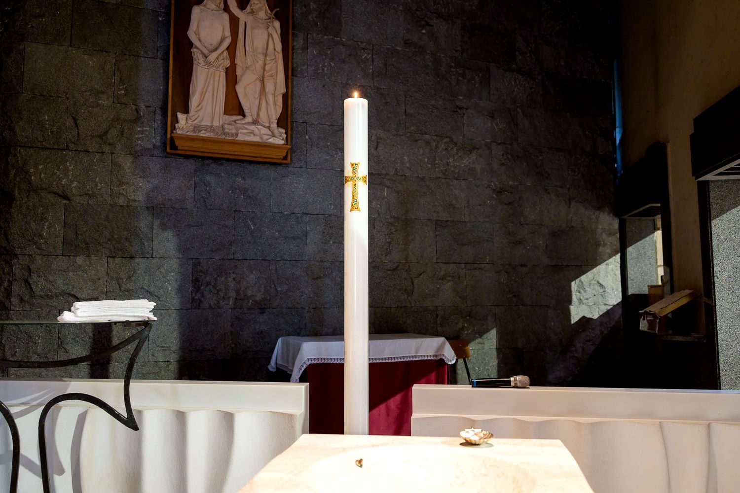 White altar candle with gold cross in a stone church sanctuary.