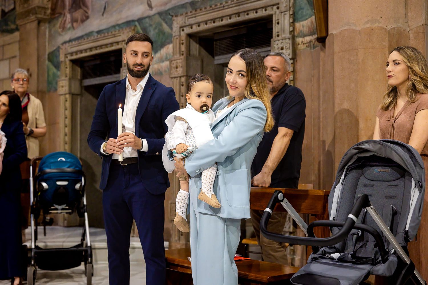 Family gathered in a historic church for a baptism ceremony, mother holding baby dressed in white.
