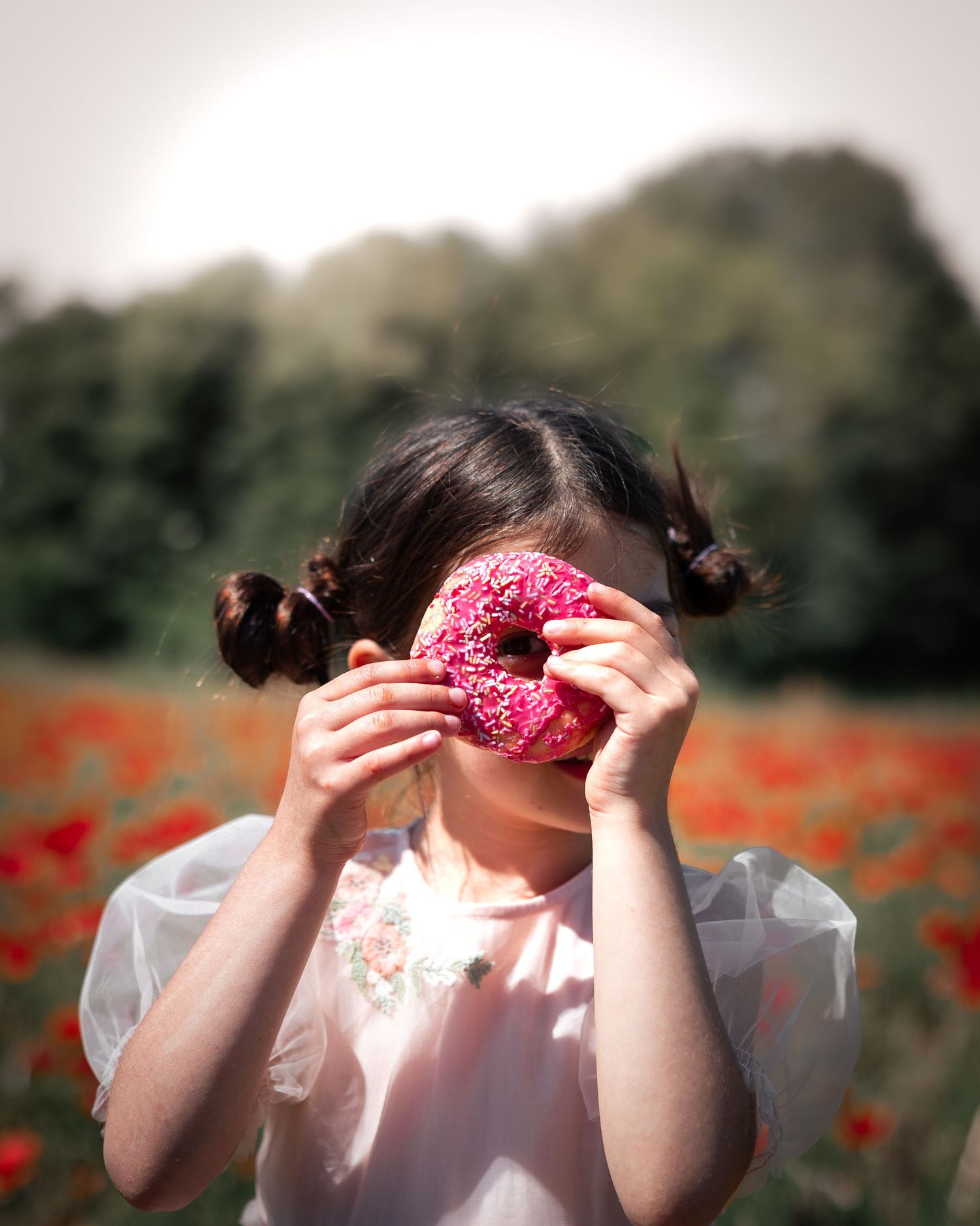 Playful scene in a poppy field with pink donuts held up to eyes.