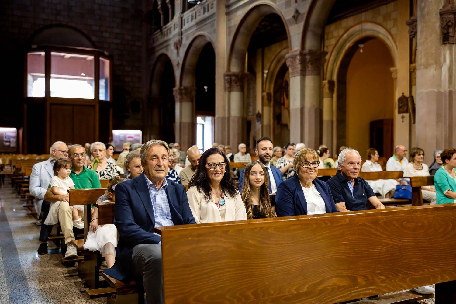 Congregation seated in wooden pews inside a grand church with arched ceilings during a religious ceremony.