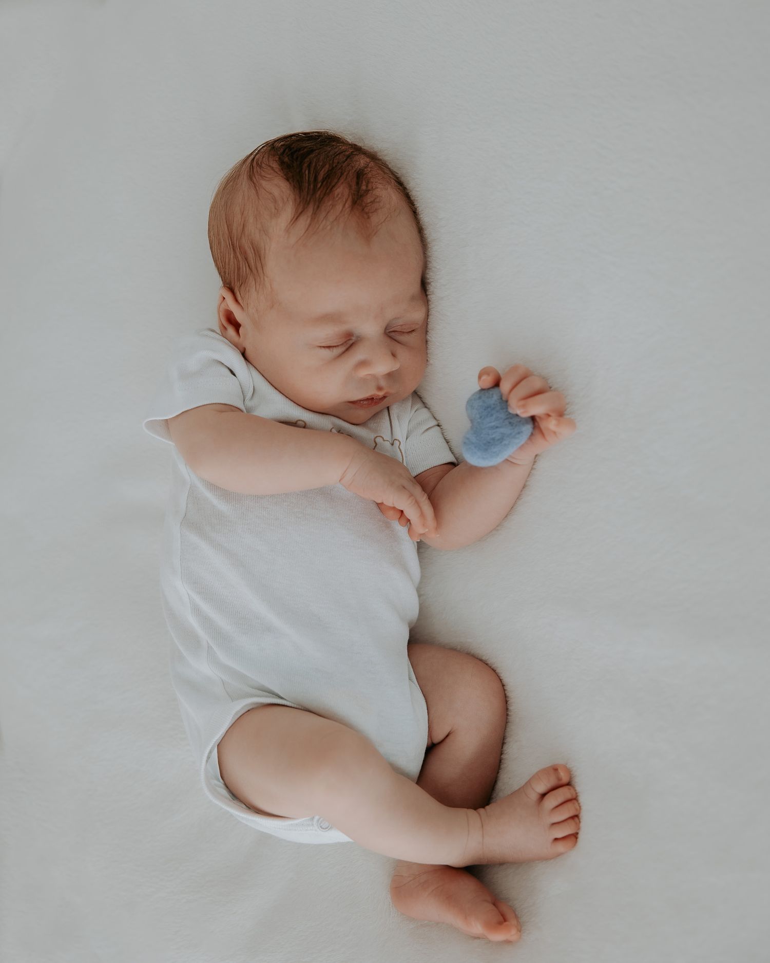 Neonato che dorme con piccolo cuore azzurro tra le mani.