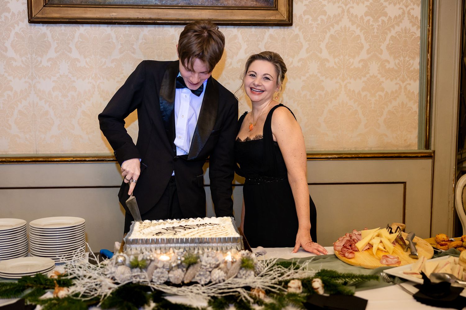 Elegant couple in formal attire cutting a decorated white cake at a sophisticated event or celebration.