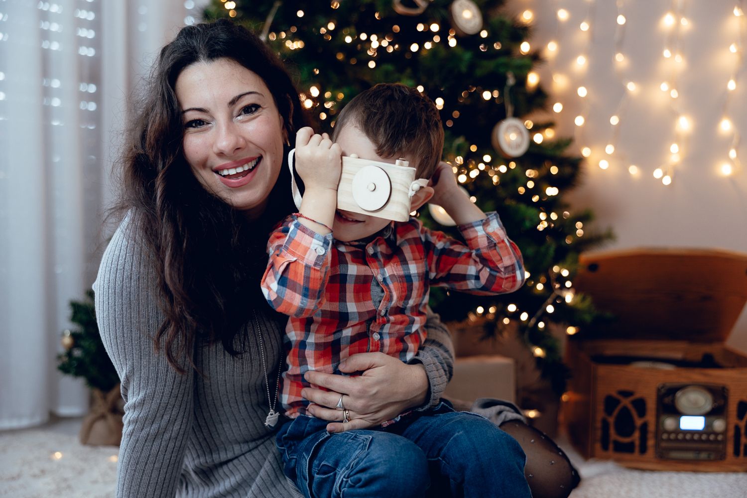 Holiday family photoshoot with decorated Christmas tree and string lights in background.