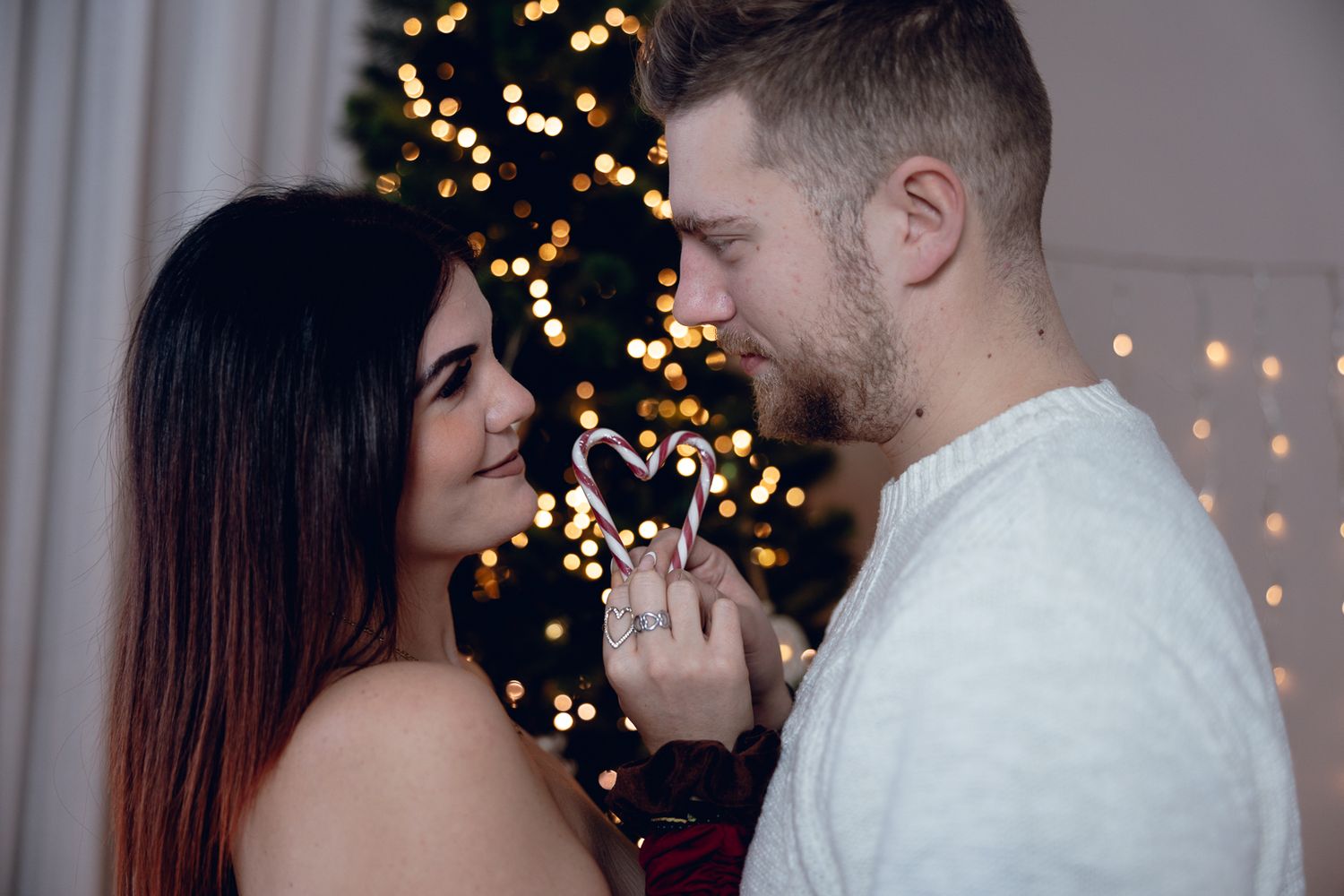 Romantic couple sharing intimate moments in front of twinkling Christmas lights and holiday decorations.