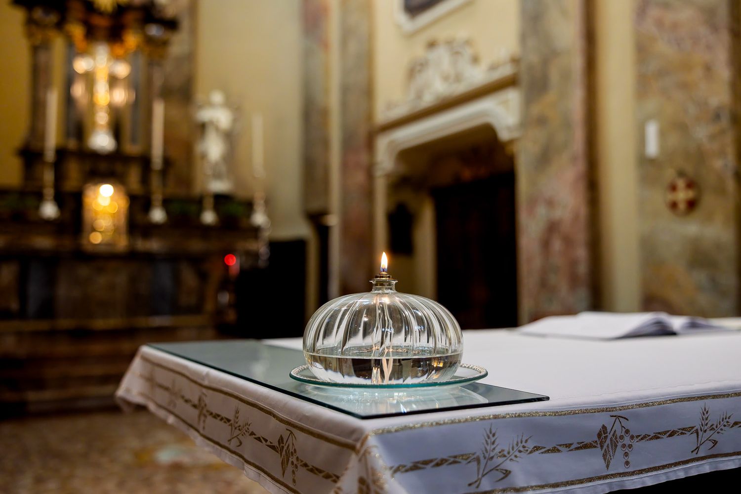 A lit candle under a glass dome on an altar inside an ornate Catholic church.