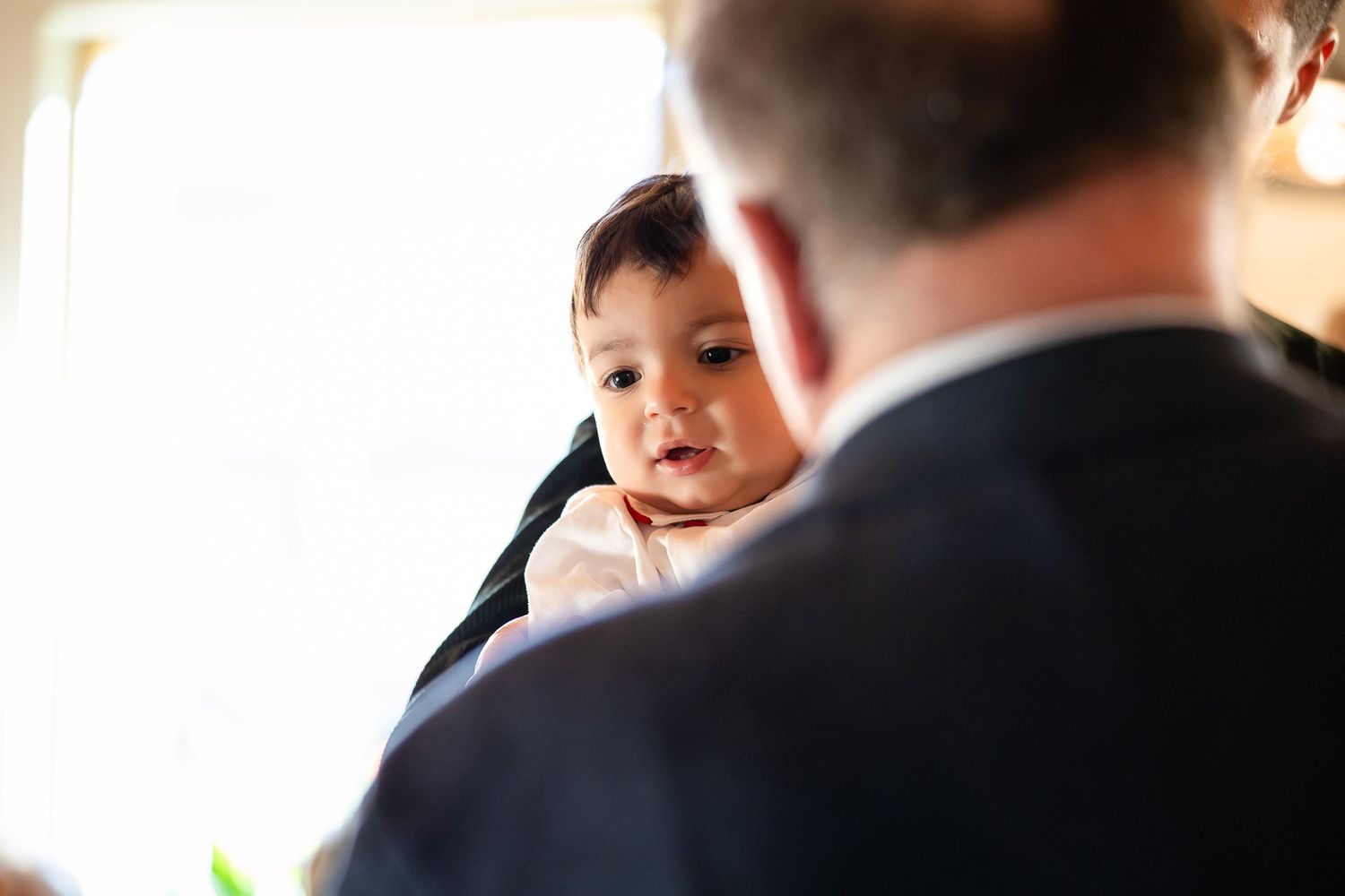Man in suit gently holding a curious baby at a formal indoor event.