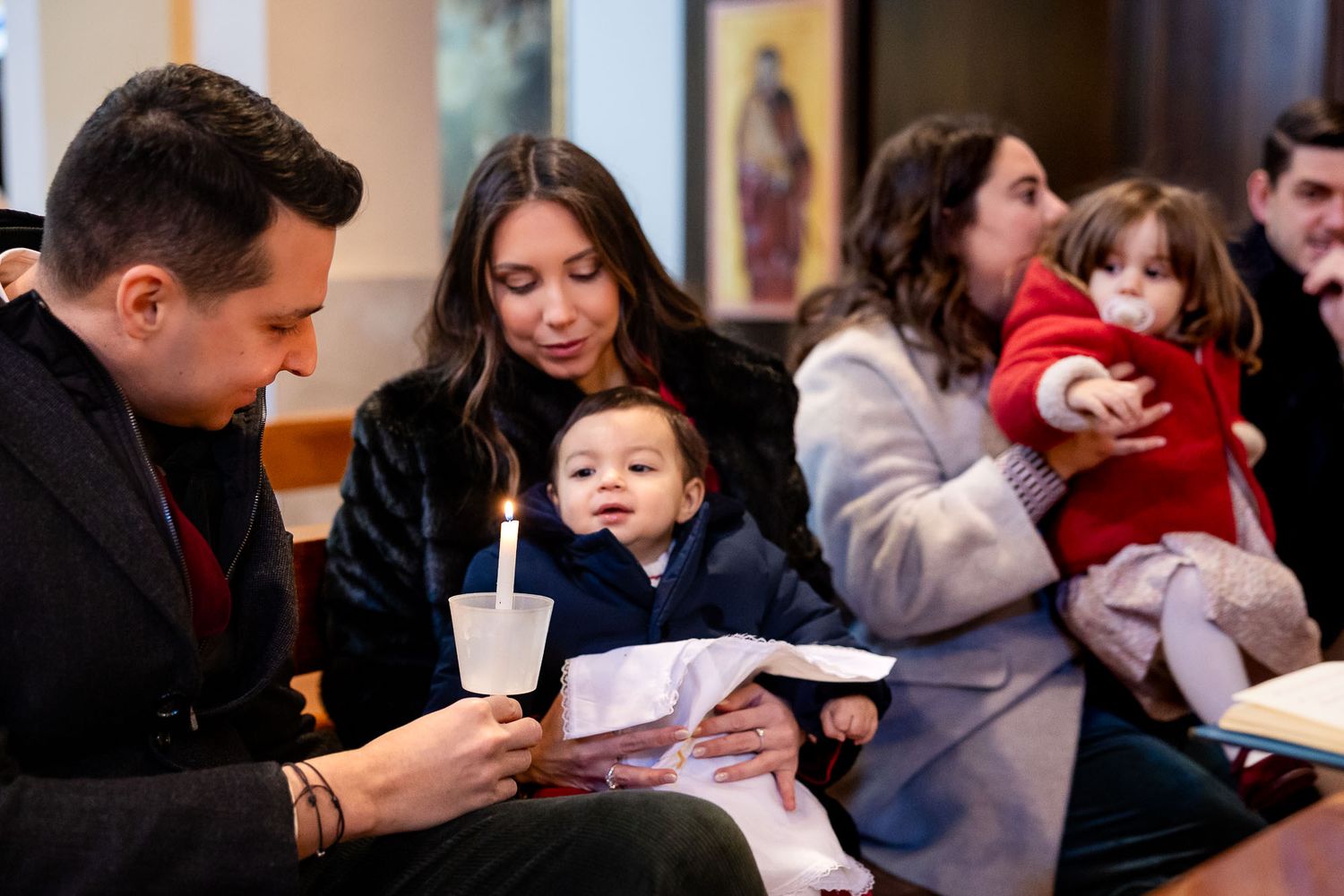 Family with baby attending a church ceremony, holding a candle and booklet during a religious service.