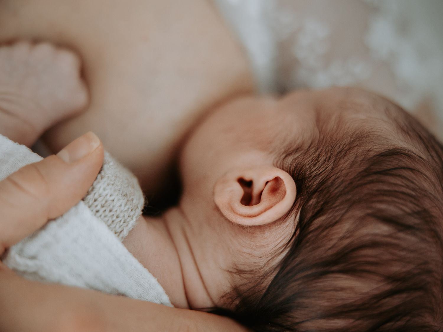 Close-up of a newborn baby with brown hair breastfeeding, showcasing the infant's delicate ear and soft skin.