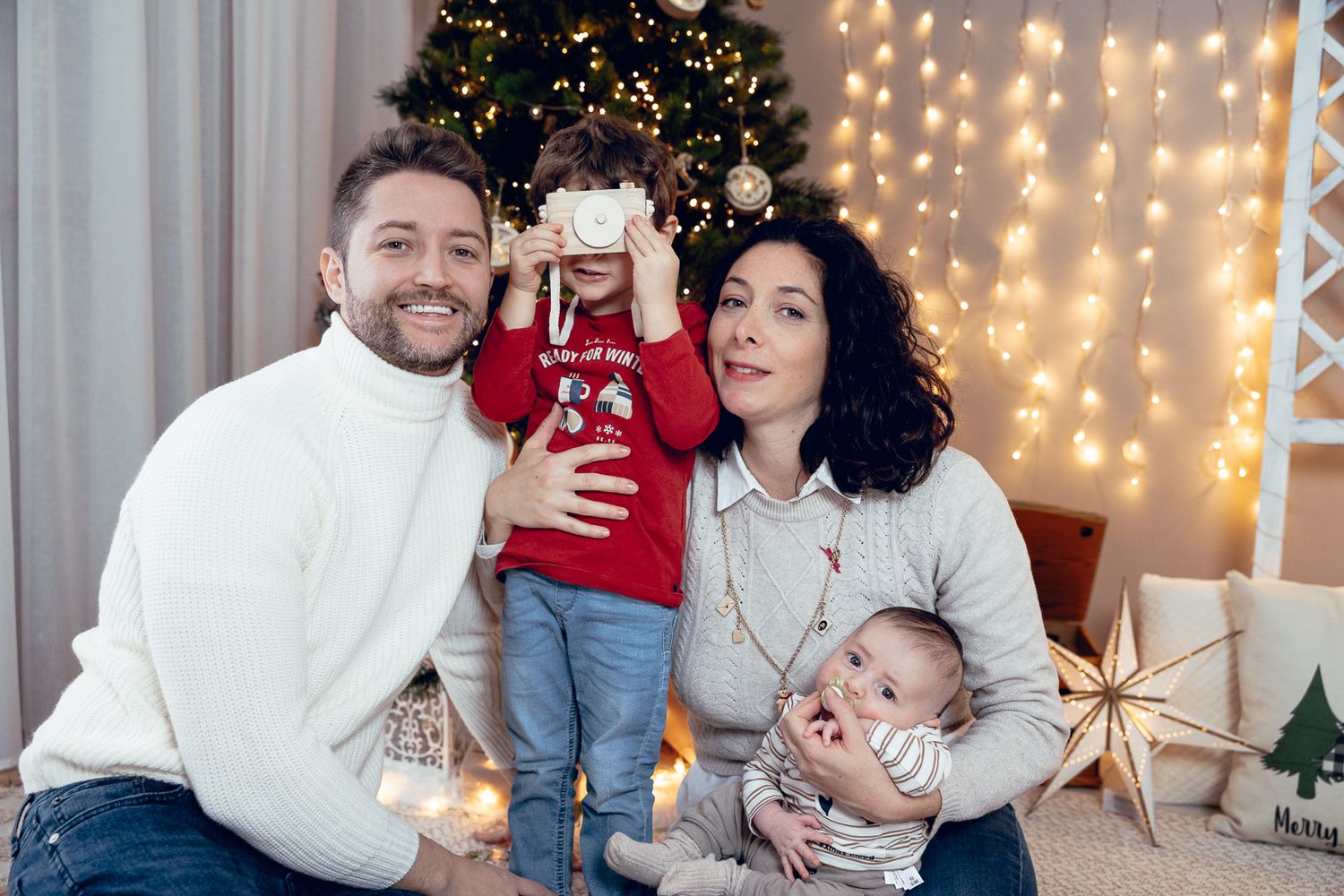 Festive family Christmas portraits with decorated tree and string light backdrop.