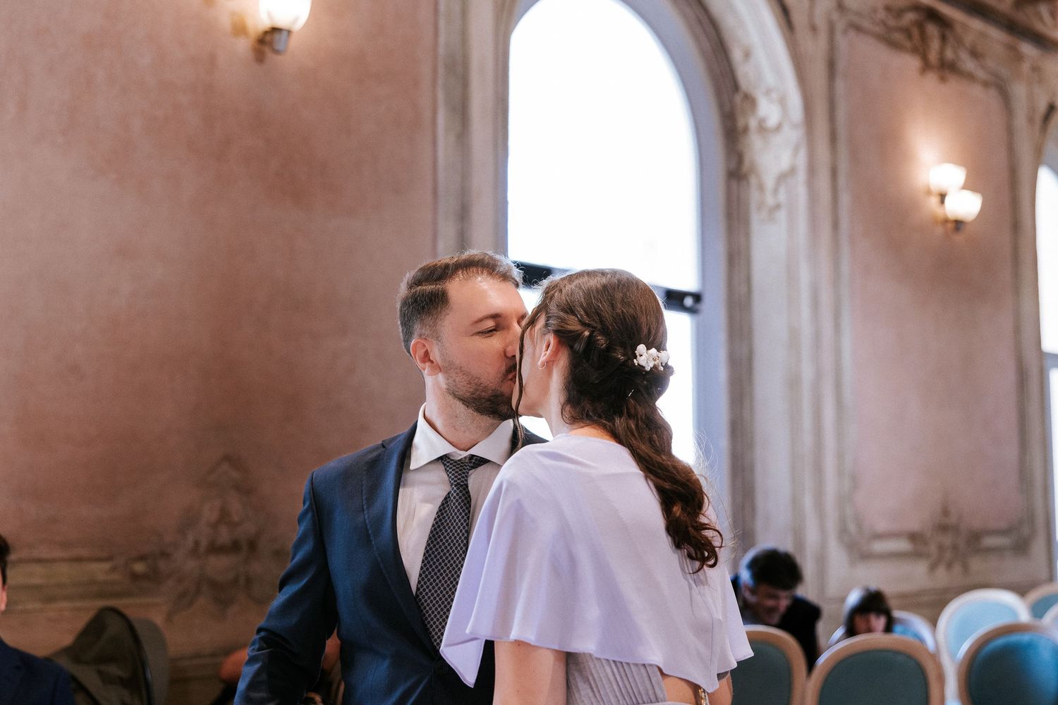 Couple shares romantic first dance in elegant ballroom with ornate pink walls and chandeliers.