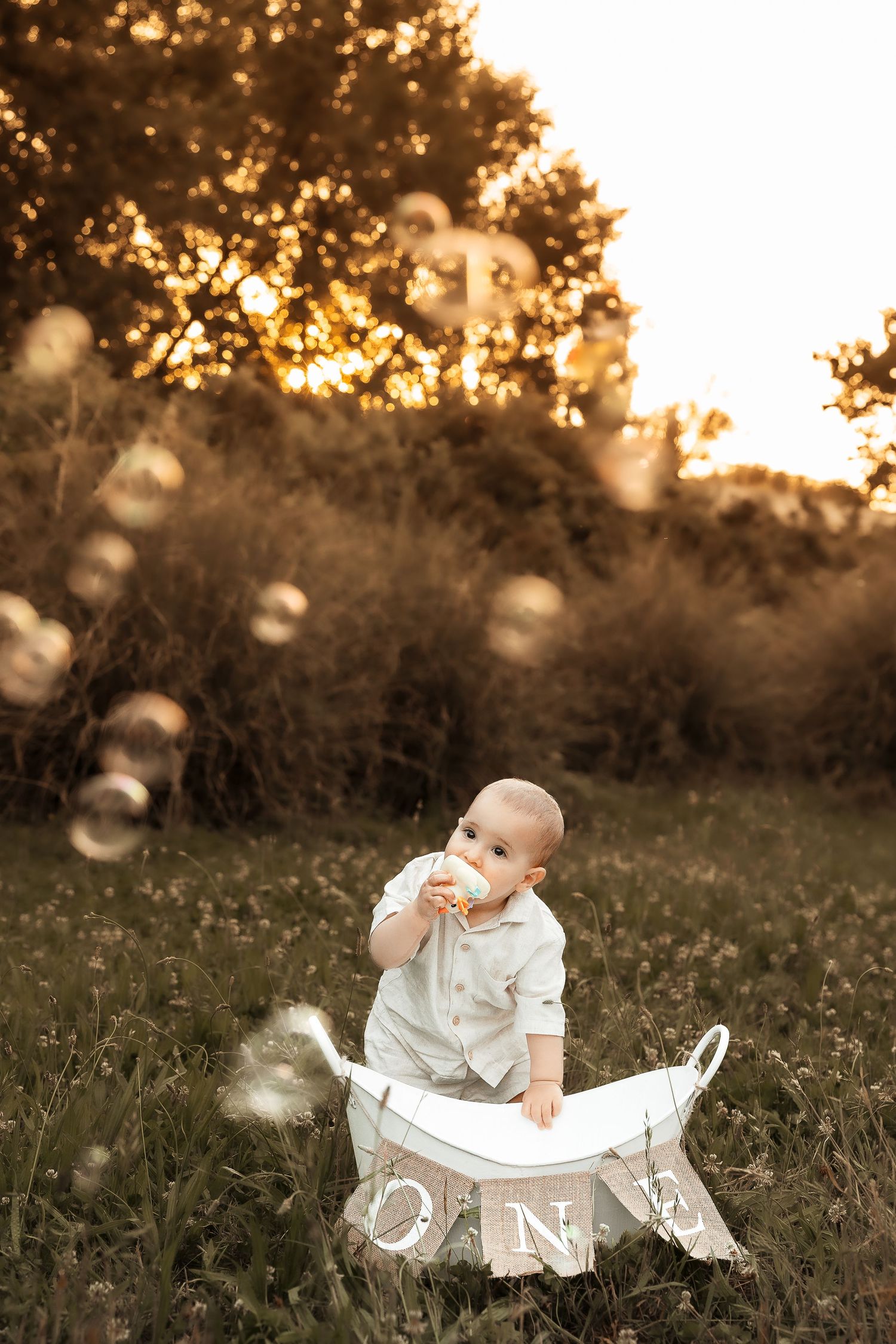 Baby's first birthday outdoor photo with bubbles, sitting in white wooden ONE crate at golden sunset.