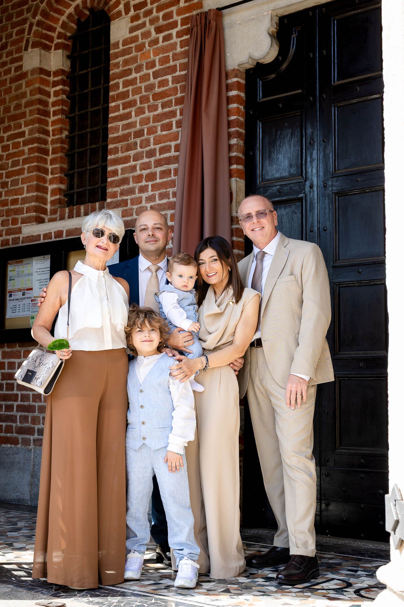 Multi-generational family posing together in elegant attire outside a brick church during a special celebration.