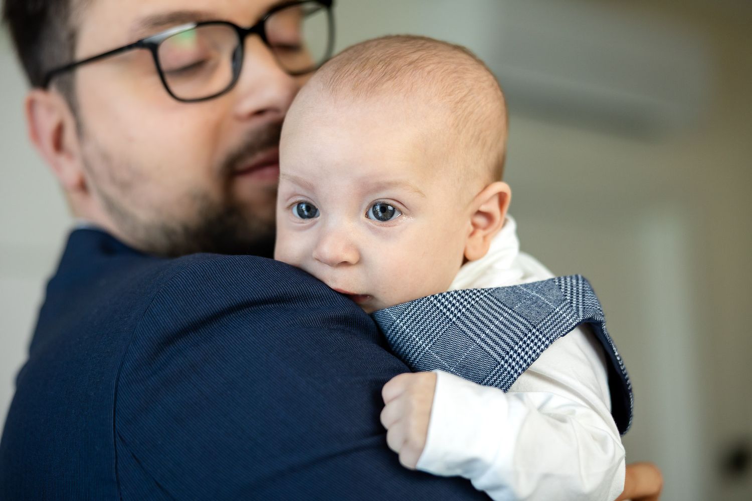 Father with glasses tenderly holding his newborn baby against his shoulder indoors.