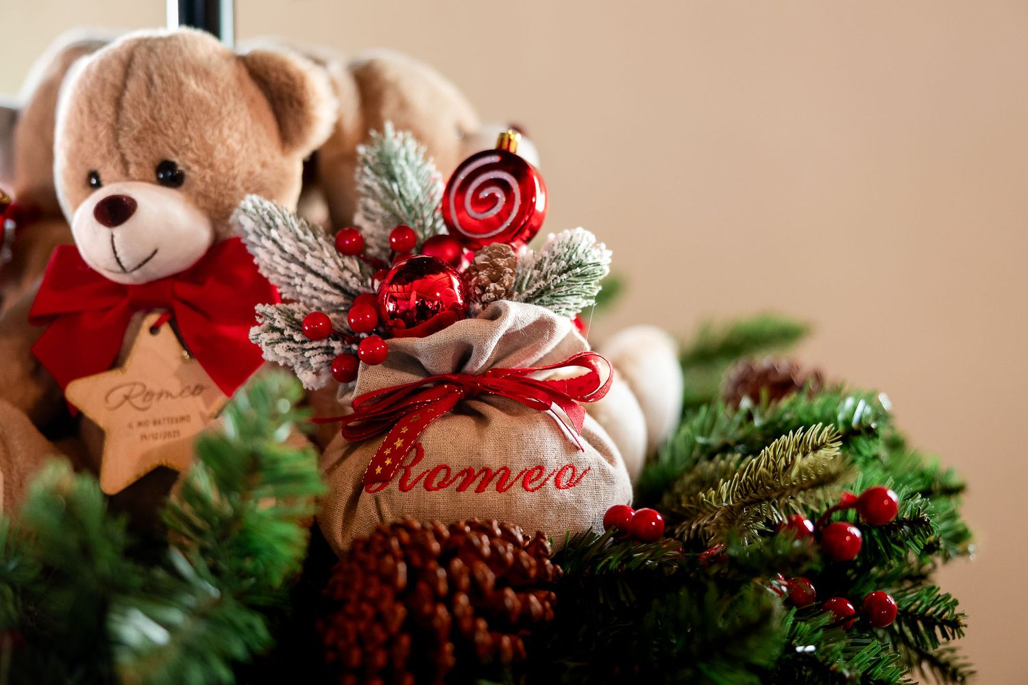 A festive Christmas arrangement featuring a teddy bear, a burlap gift bag labeled Romeo, red berries, and pine branches.
