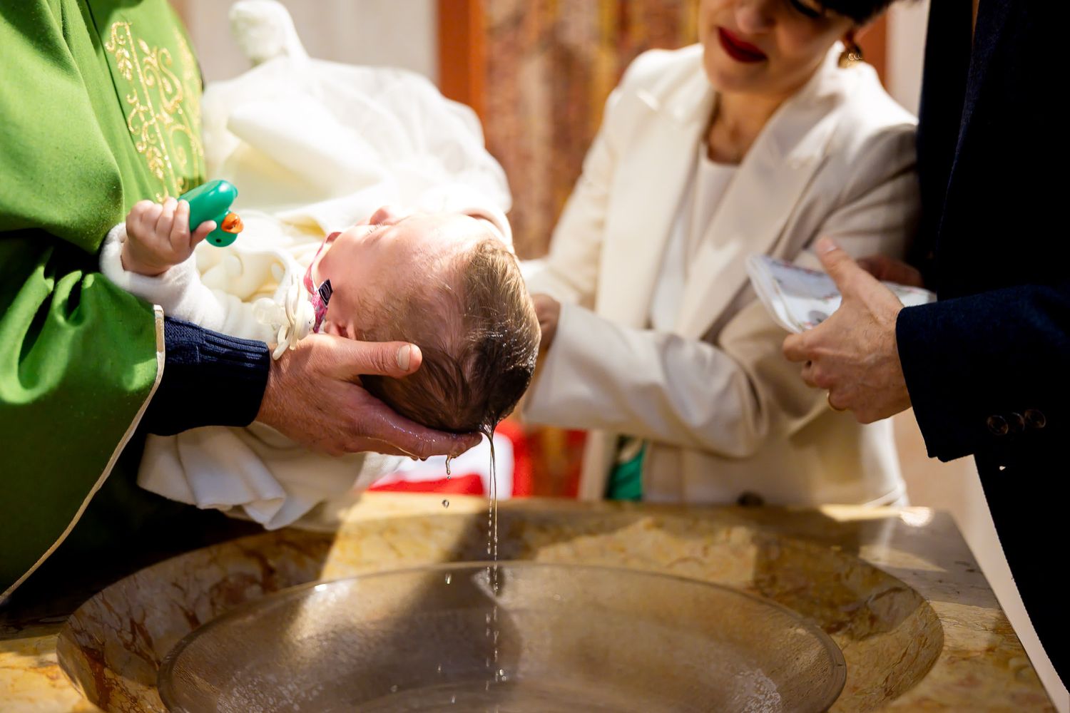 A priest baptizes a newborn baby by pouring water over its head at a traditional Christian baptism ceremony.