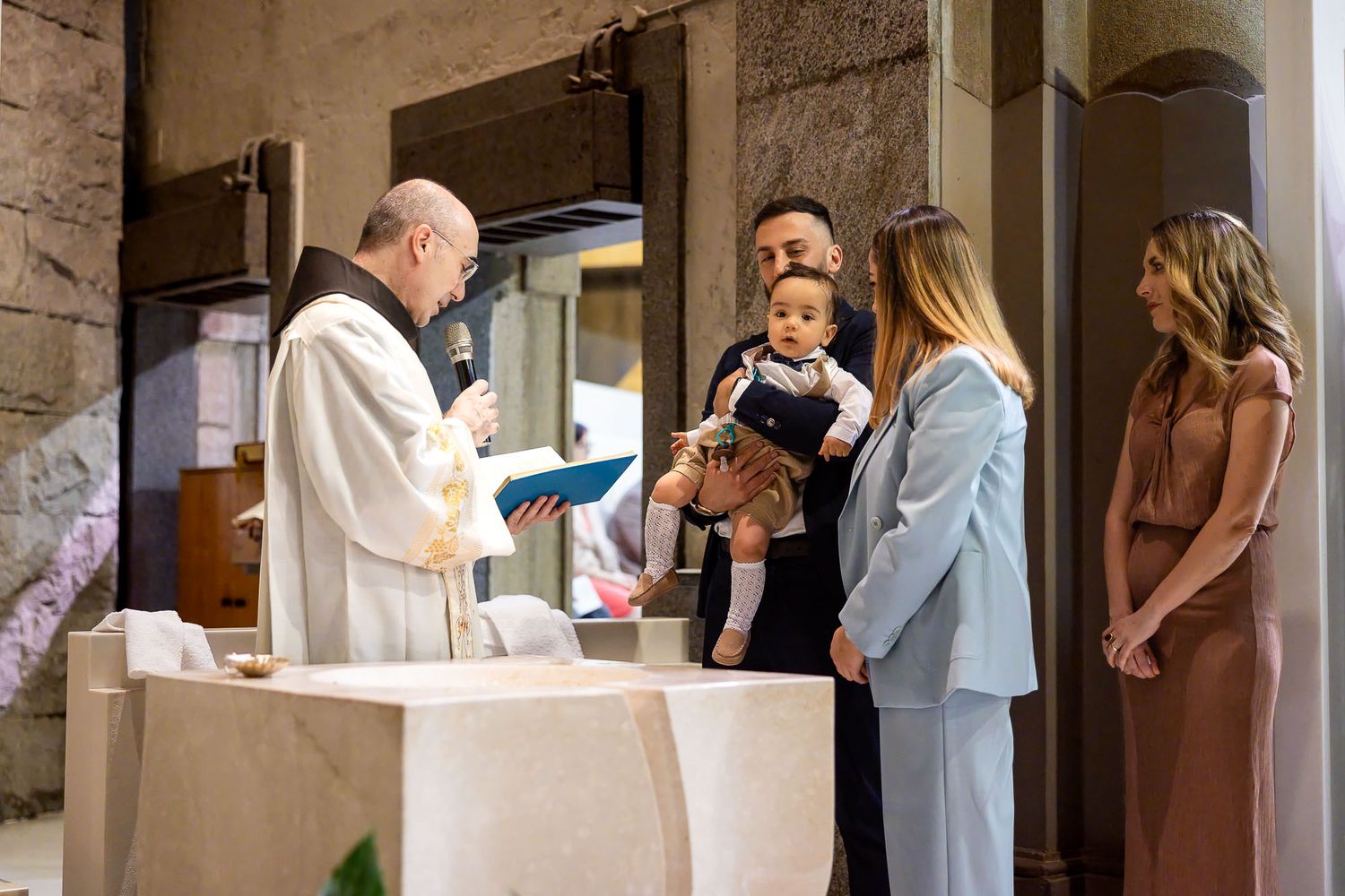 Priest performs a baptism ceremony with parents holding their baby at a church altar.