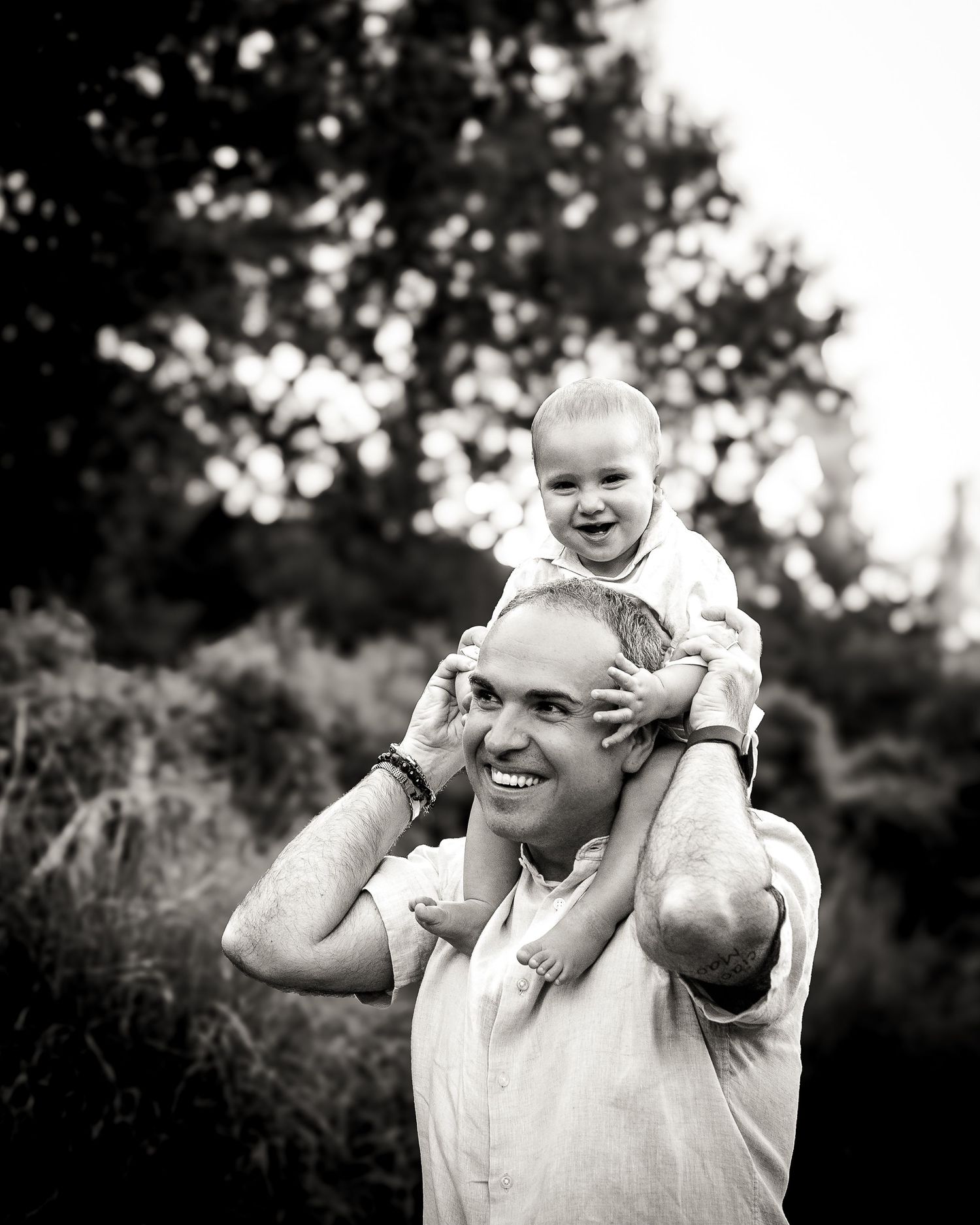 Papà che tiene il bambino sulle spalle durante un servizio fotografico naturale per il primo compleanno