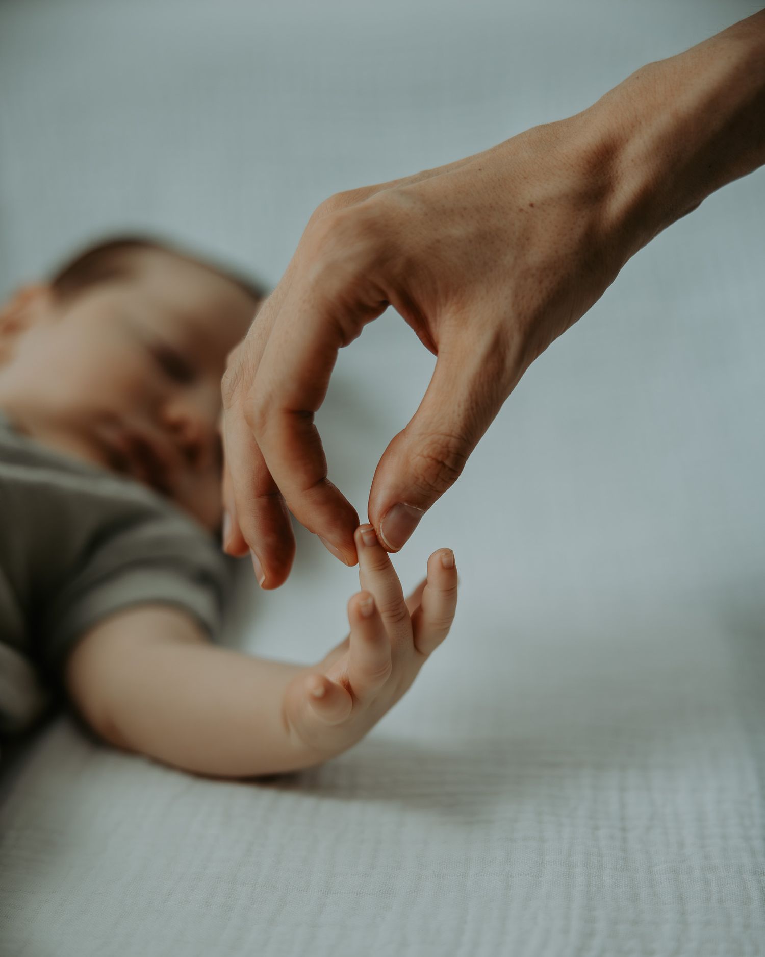 Close-up view of hands gently touching and creating a soft, intimate connection against a muted background.