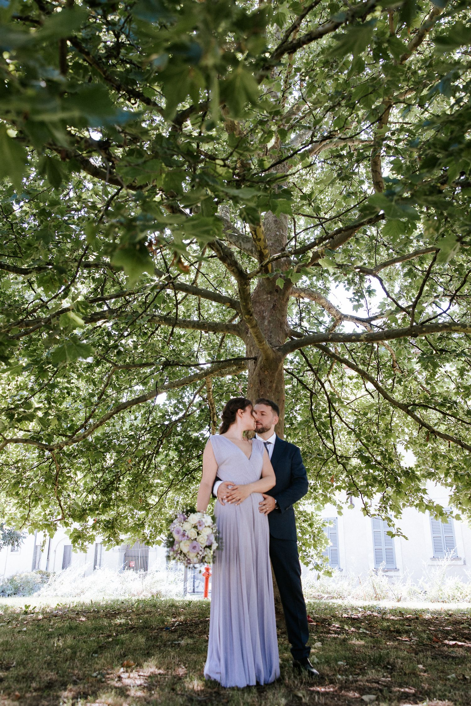 A romantic moment captured under a lush green tree canopy on a sunny day.