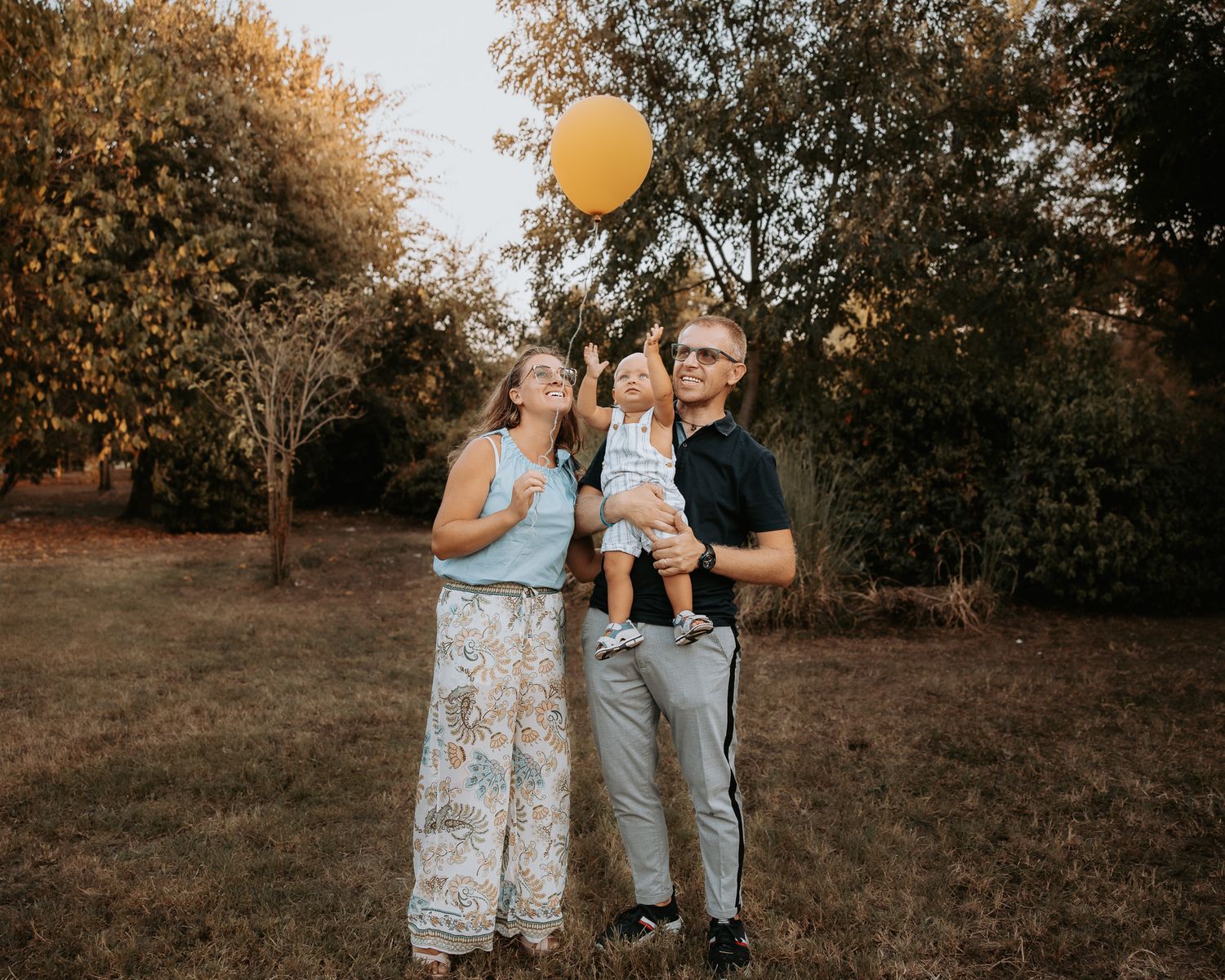 Family photo session in a golden autumn field with yellow balloons at sunset.