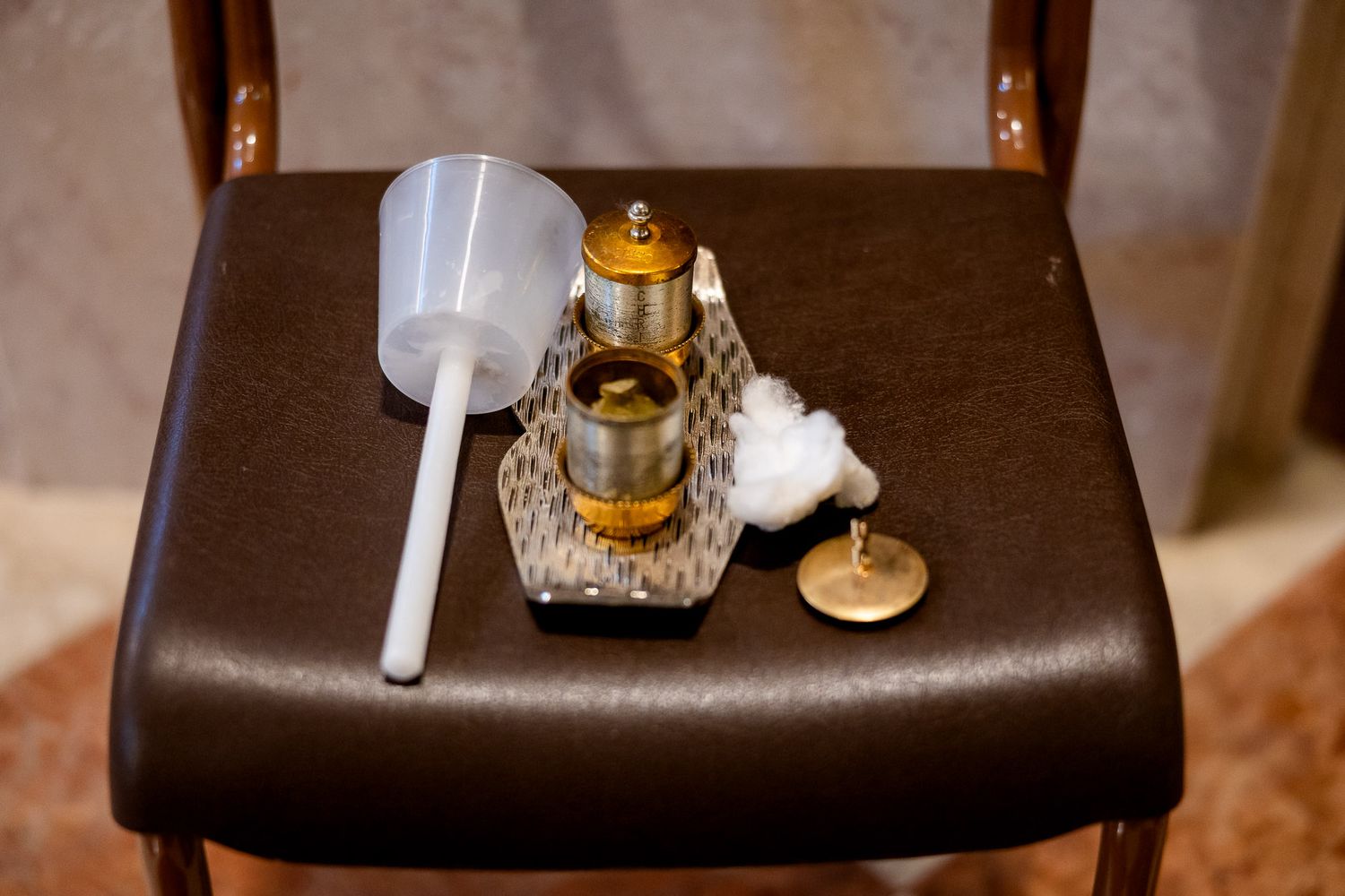 Gold ornate oil lamp with cotton wick, plastic funnel, and lid on a brown leather chair.