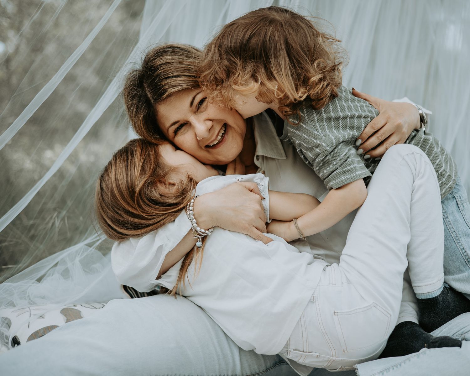 Intimate family moment captured on white bedding with soft lighting.